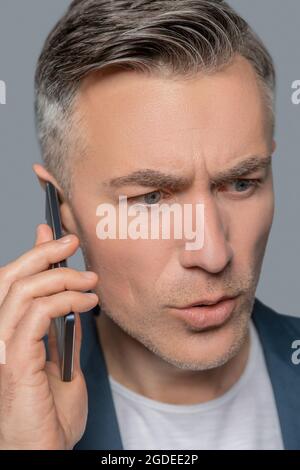 Serious alarmed man with smartphone near ear Stock Photo