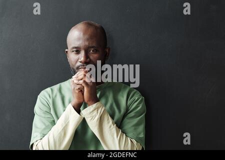 Portrait of African pensive man looking at camera standing against the black background Stock Photo