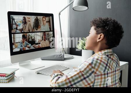 African schoolboy sitting at desk in front of computer and talking online with his classmates and teacher, he studying online Stock Photo