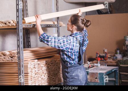 Female apprentice checking wooden plank at carpentry workshop Stock Photo