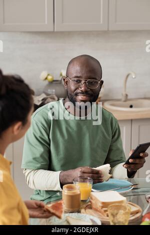 African young man talking to his wife while they sitting at the table and having breakfast Stock Photo