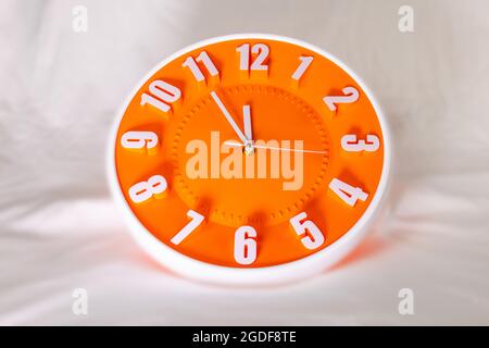 Orange Wall Clock on white blur background. Shadows over the clock face. Watch show the time. Clock face with white time pointer and numbers. Times up Stock Photo