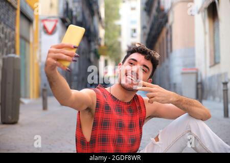 Young caucasian man with long false nails taking a selfie sitting on the floor. Stock Photo
