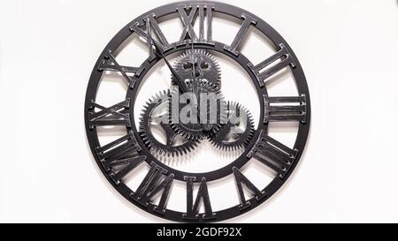 Black metal Wall Clock. Shadows over the clock face. Gears in the middle of the clock. Old antique metal. Watch show how the time. Rustic black watch