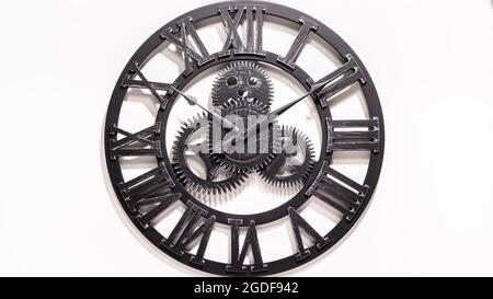 Black metal Wall Clock. Shadows over the clock face. Gears in the middle of the clock. Old antique metal. Watch show how the time. Rustic black watch Stock Photo