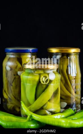 In this photoillustration, homemade pickled chili peppers in glass jars on black background Stock Photo