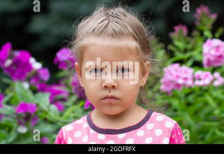 Portrait of frowning caucasian girl of four years old looking at camera in summer park Stock Photo