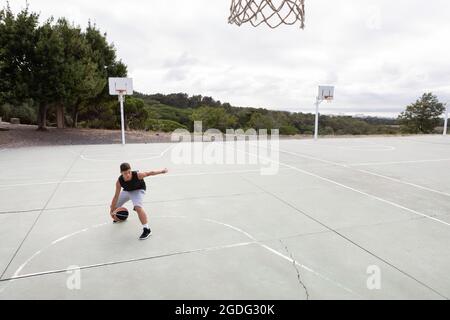 Male teenage basketball player practicing with ball near basketball hoop Stock Photo