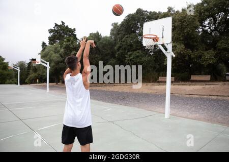 Male teenage basketball player throwing ball toward basketball hoop Stock Photo