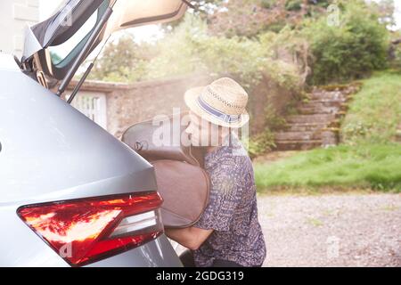 Young man in trilby removing luggage from car boot outside hotel Stock Photo