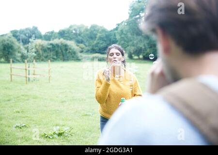 Couple playing with soap bubbles in field Stock Photo