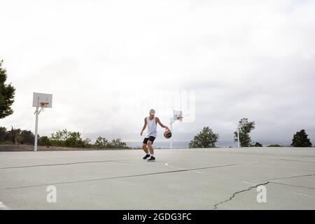 Active teenager basketball player practicing with ball on street court ...