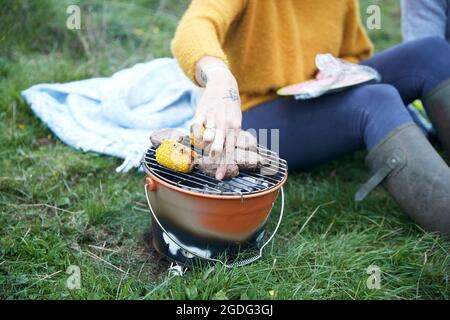 Woman and boyfriend sitting in rural field cooking on barbecue grill, cropped Stock Photo