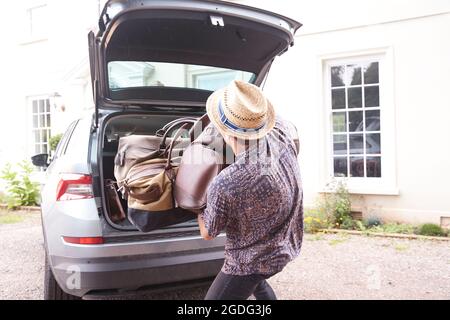 Young man in trilby removing luggage from car boot outside hotel, rear view Stock Photo