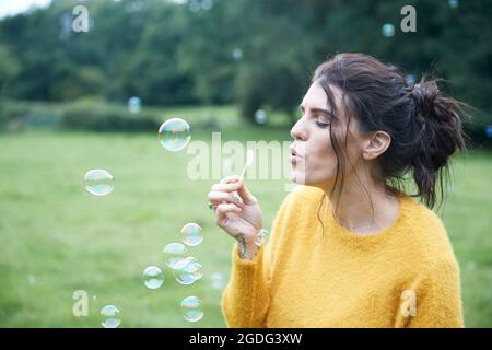 Woman playing with soap bubbles in field Stock Photo