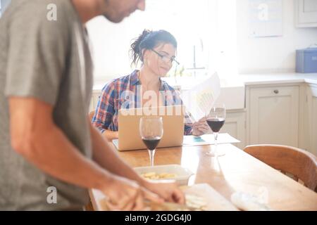 Man preparing vegetables at kitchen table, girlfriend reading paperwork Stock Photo