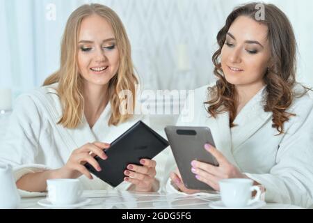 Two beautiful young women in bathrobes using digital devices Stock Photo