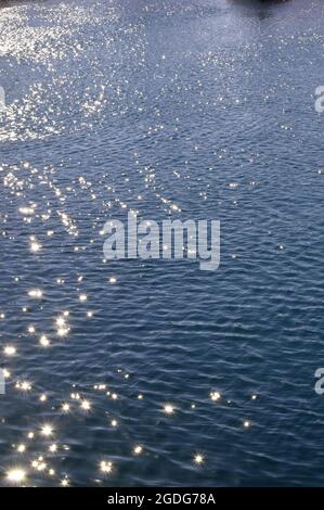 Blue sea water with sun reflections and ripples. Blue sea water surface with ripples and sun reflections. Sparks from the sun's reflection on the blue Stock Photo