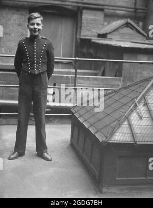 1940s, historical, a hotel bellboy in his uniform standing on a flat roofed area beside an air vent, London, England, UK. A bellboy was traditionally an adolescent male, hence the tern bellboy, who was on call to run general errands and to be of assistance for guests during their stay, as well carrying luggage to and from their rooms, when they checked in and out. Stock Photo