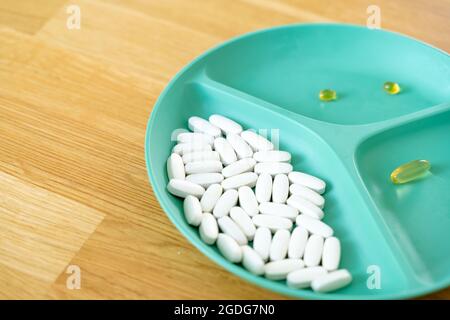 Green plate with dividers filled with pills and capsules. Biohacking movement. Wellbeing concept. Modern medicine with antibiotics. Stock Photo