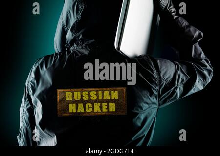 Russian hacker with a laptop on his shoulder on a dark background. The concept of risk of Russian hackers in political affairs of European and America Stock Photo
