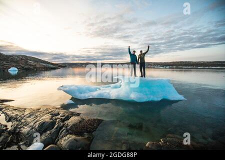 Couple standing on iceberg with arms raised in celebration Stock Photo
