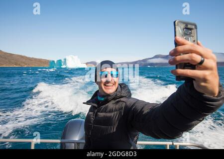 Traveller takes a selfie with iceberg from boat. Stock Photo