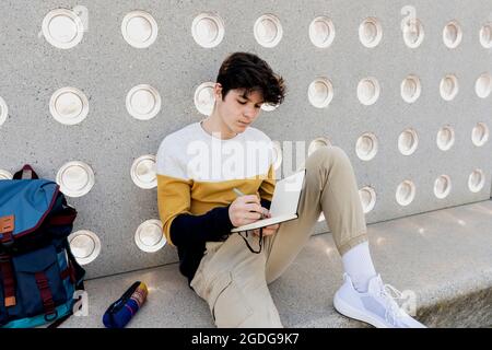 Young male writing notes in a notebook sitting on a bench Stock Photo