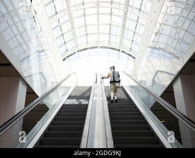 Rear view of a young teen with backpack moving up on escalator Stock Photo