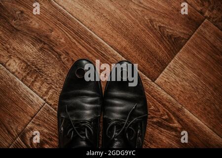 Men classic fashion formal black shoes. boots on a brown textured wooden floor. engagement gold silver rings lying on groom shoes Stock Photo