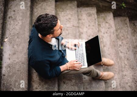 businessman using laptop computer sitting on steps in city Stock Photo