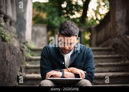 Man with laptop looking at watch sitting on steps in city Stock Photo