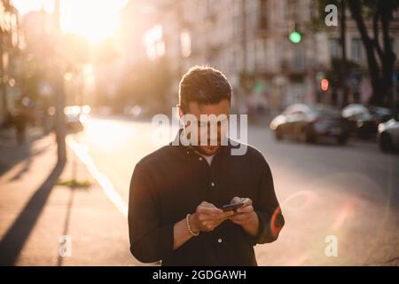 Happy man using smart phone standing on street in city during summer Stock Photo