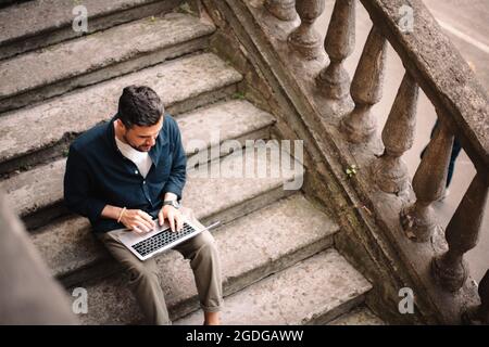 Man using laptop computer sitting on steps in city Stock Photo