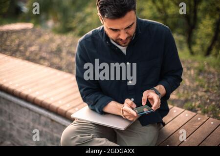 businessman using smart phone while sitting on bench in park Stock Photo