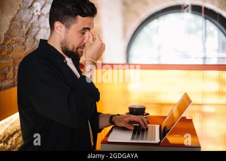 Tired man using laptop computer at cafe Stock Photo