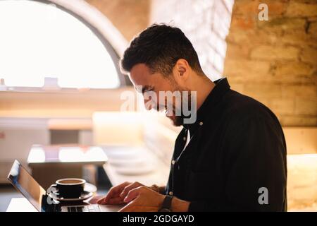 Happy man laughing while using laptop computer at cafe Stock Photo