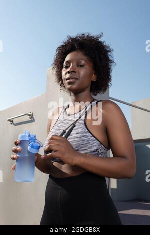 Black female athlete with jumping rope and water looking at camera during break Stock Photo