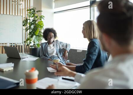 Happy black female manager smiling and talking with coworkers during conference Stock Photo