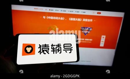 Person holding cellphone with logo of Chinese online education platform Yuanfudao on screen in front of business webpage. Focus on phone display. Stock Photo