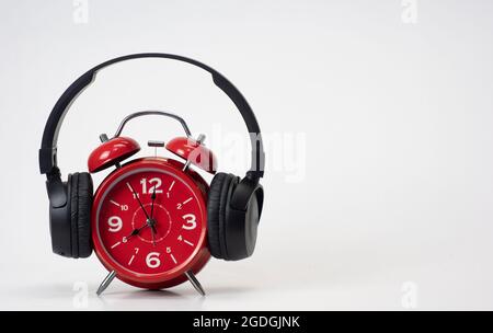 Red Alarm Clock put on headphones over white background, Timeless Music Concept. Copy space Stock Photo