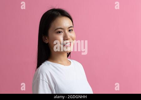 Portrait half profile turn of asian positive smiling woman on pink background. Stock Photo