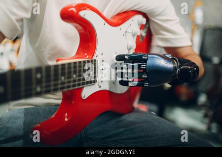 Young disabled man with artificial prosthetic hand close up plays on strings electric guitar at shop Stock Photo