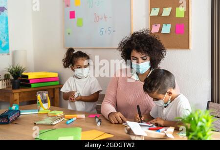 Female teacher with children drawing in preschool classroom while wearing face protective mask during corona virus pandemic Stock Photo