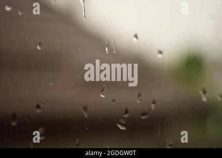 Closeup window glass in rain drops. Brown tiled roof in blurred background. Stock Photo