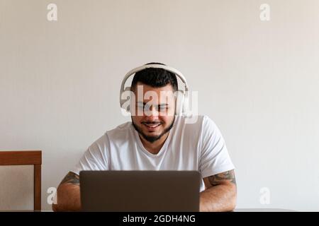 front view of a young Latino man using a laptop and headphones Stock Photo