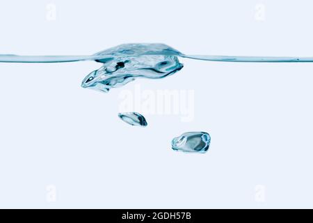 Studio shot of a small water wave and two rising air bubbles against a white background. Stock Photo