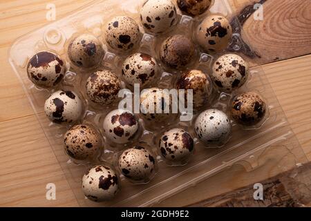 Several dietary quail eggs in a plastic box, close-up, on a wooden table, top view. Stock Photo