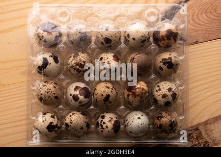 Several dietary quail eggs in a plastic box, close-up, on a wooden table, top view. Stock Photo
