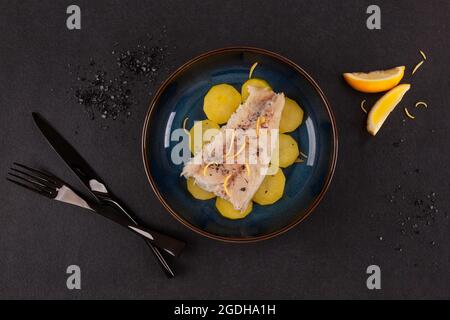 Grilled fish fillet served with potatoes on plate over black background. Culinary eating. Stock Photo